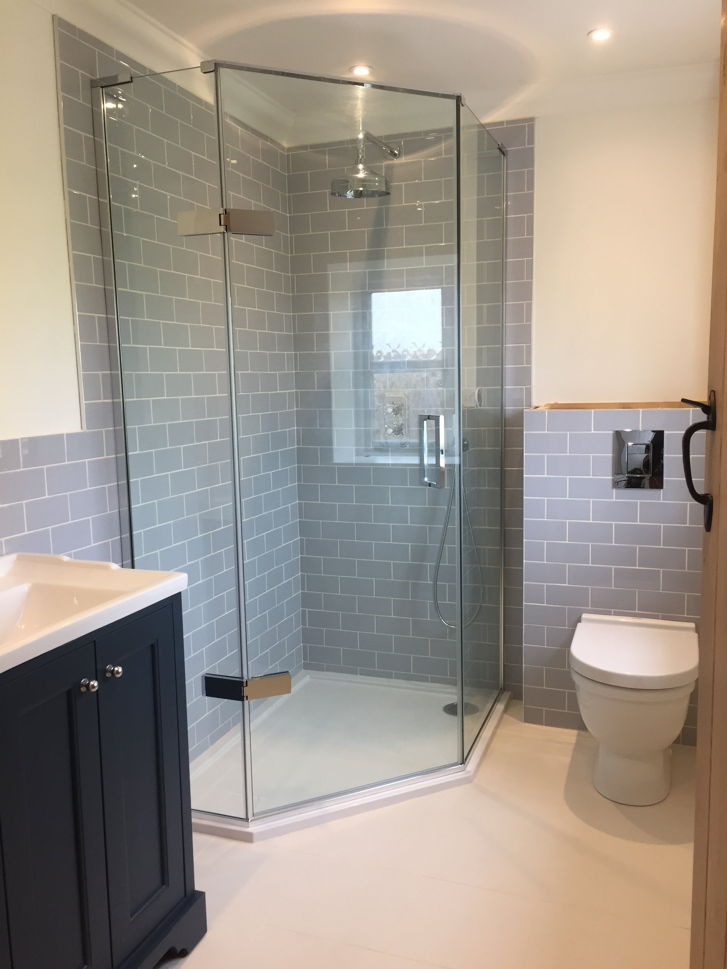 Modern bathroom with a glass-enclosed shower featuring gray subway tiles, a white toilet, and a navy blue vanity with a white countertop.