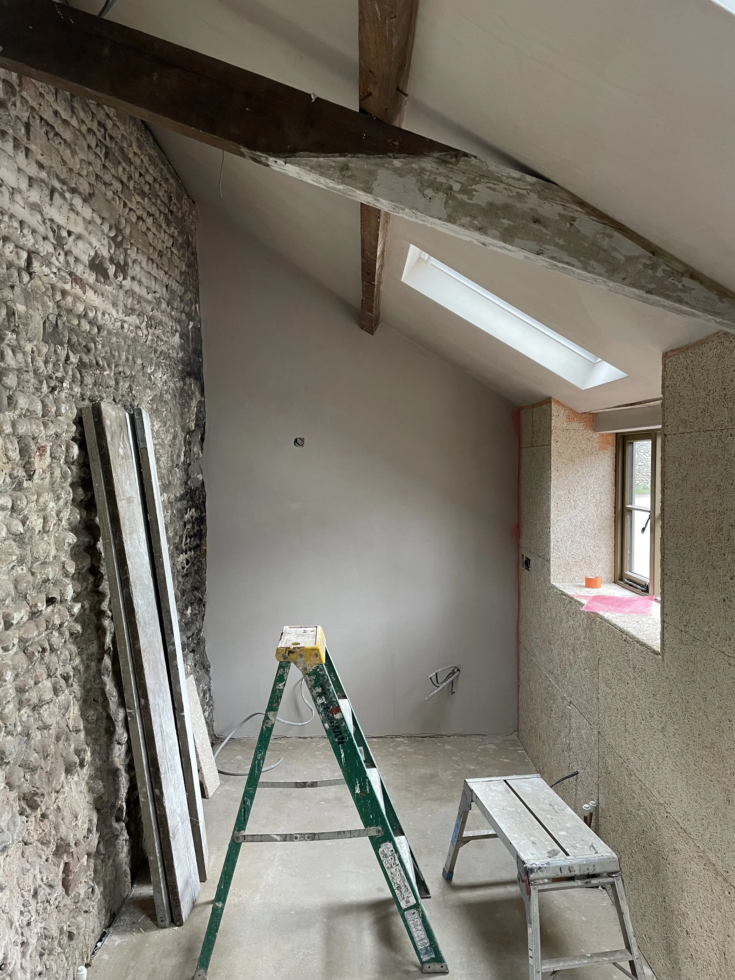 Room under renovation with exposed stone wall, ladder, work table, and window with ledge under construction.