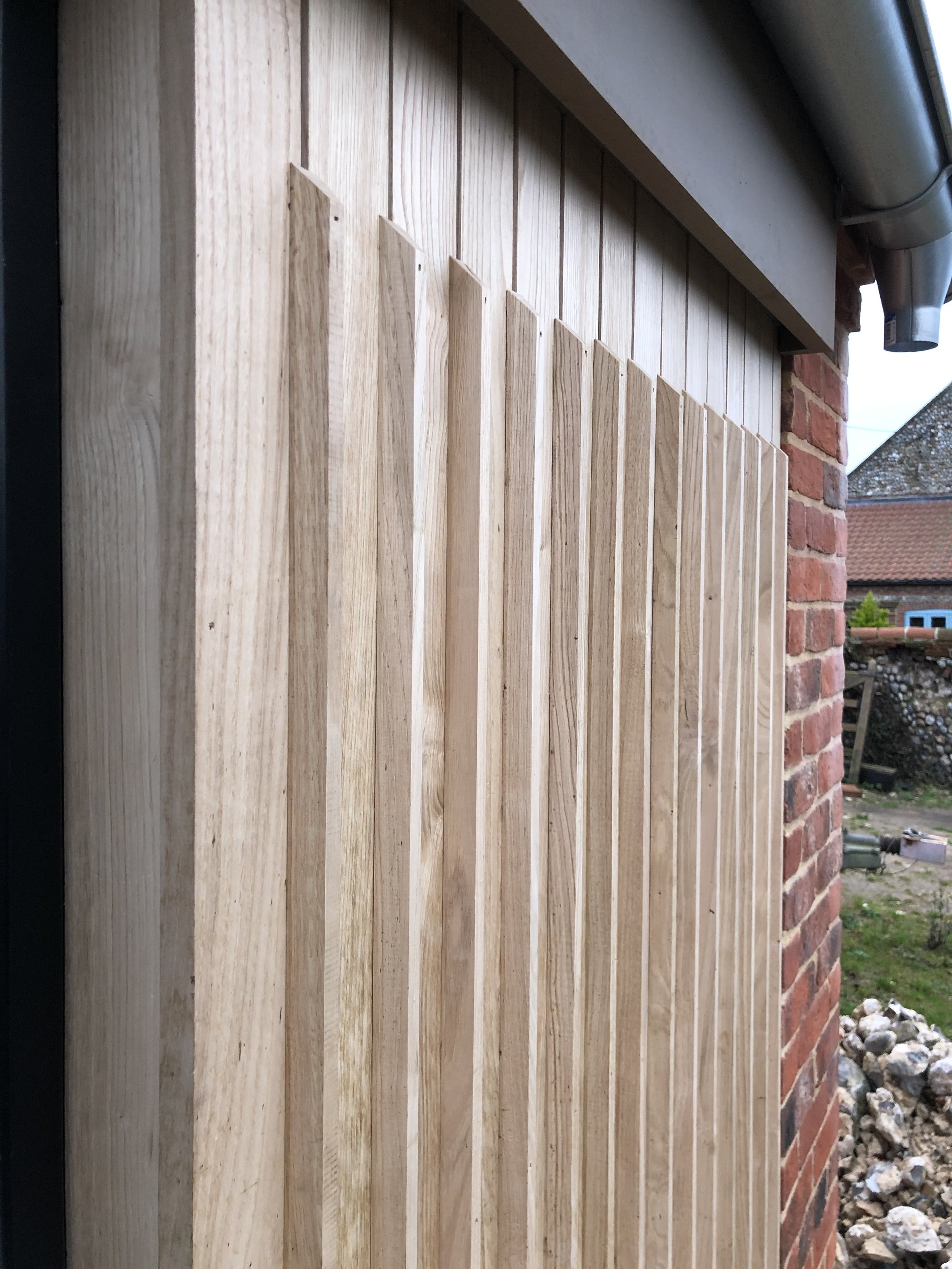 Wooden slats attached to a brick exterior wall with a gutter pipe above.
