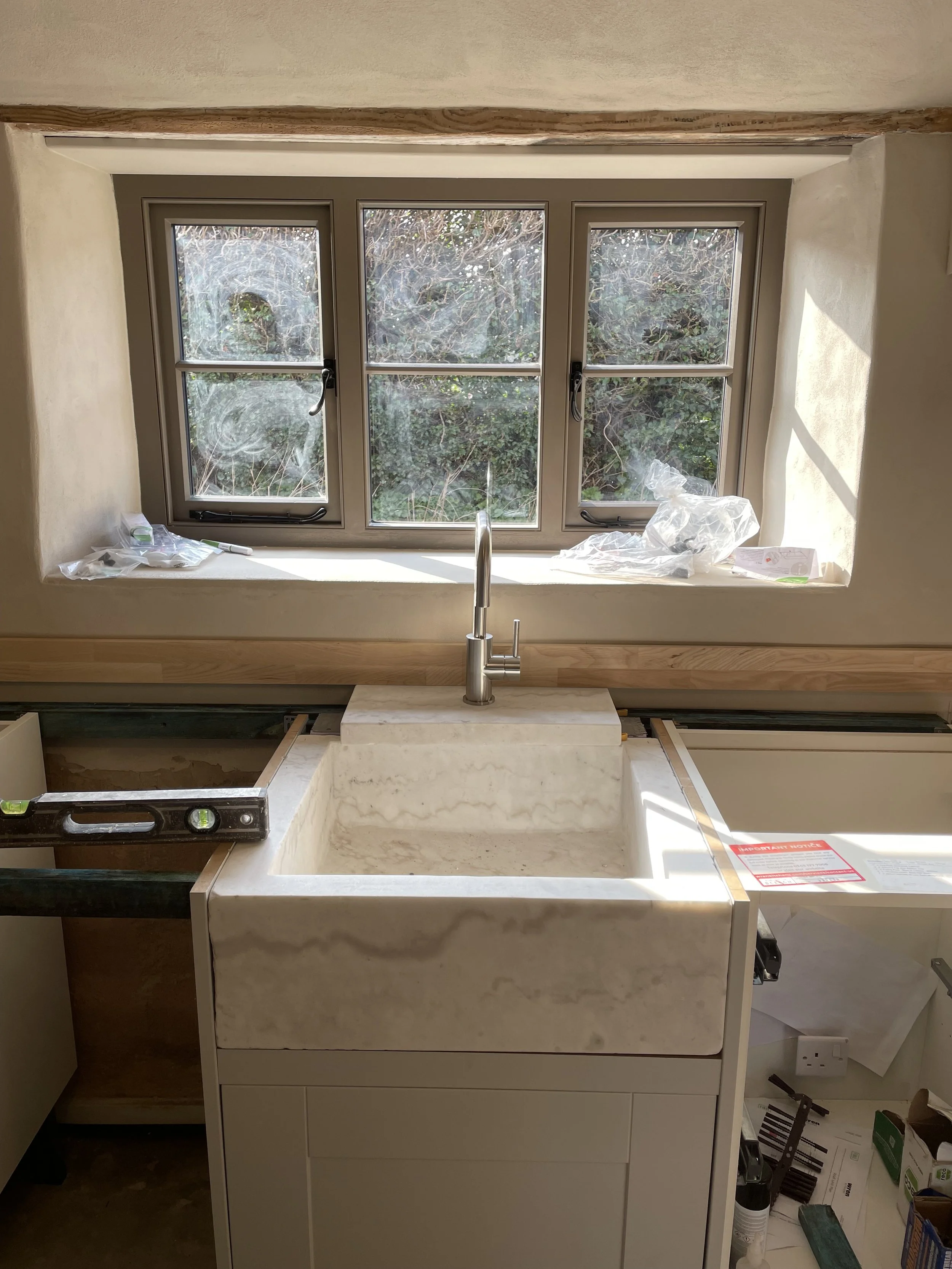 A kitchen with a large window above a marble sink counter, with tools and packaging materials around, indicating ongoing installation or renovation.