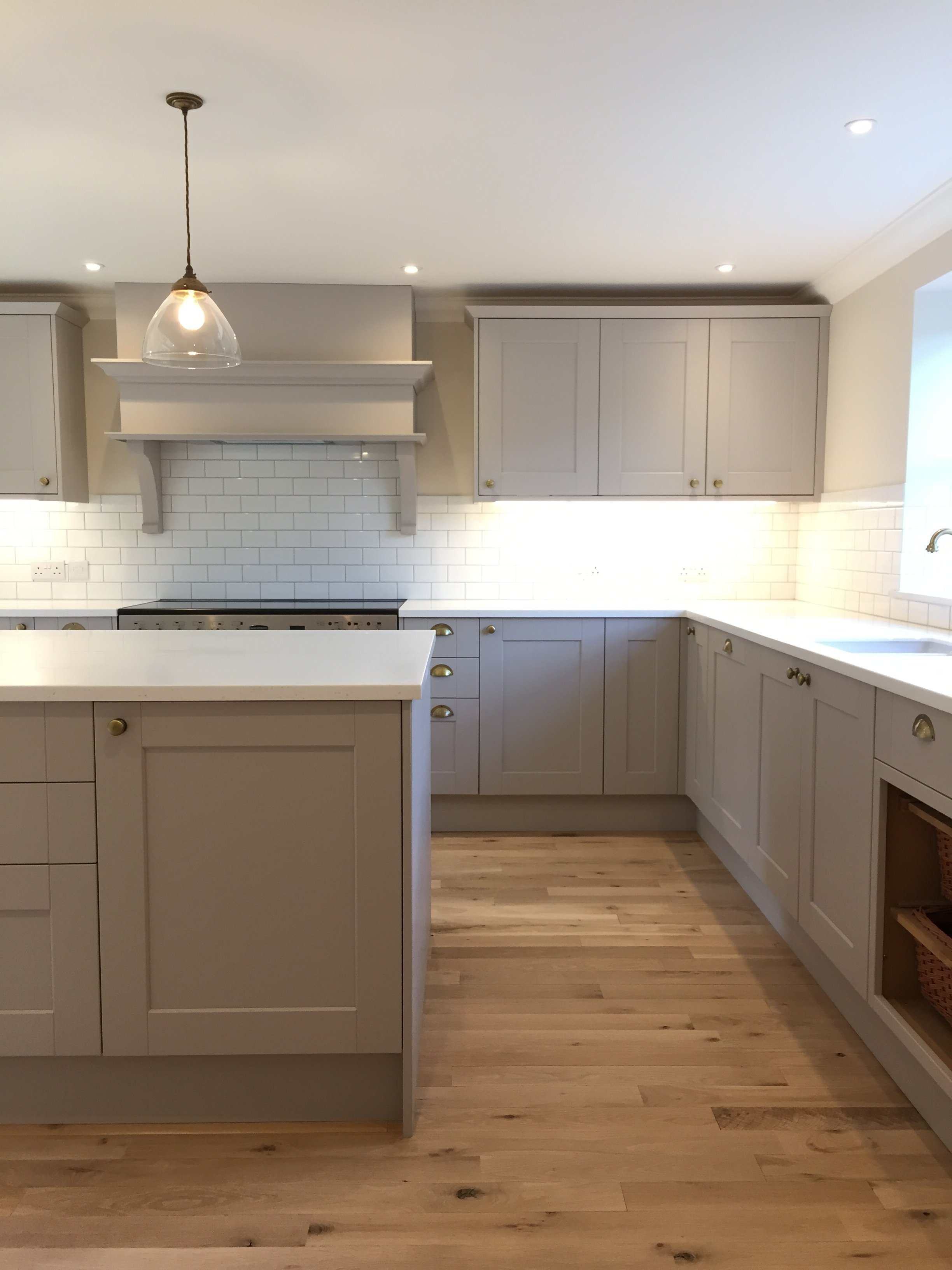A modern kitchen with white cabinets, a white island, a white subway tile backsplash, wood flooring, a hanging pendant light, and recessed ceiling lights.