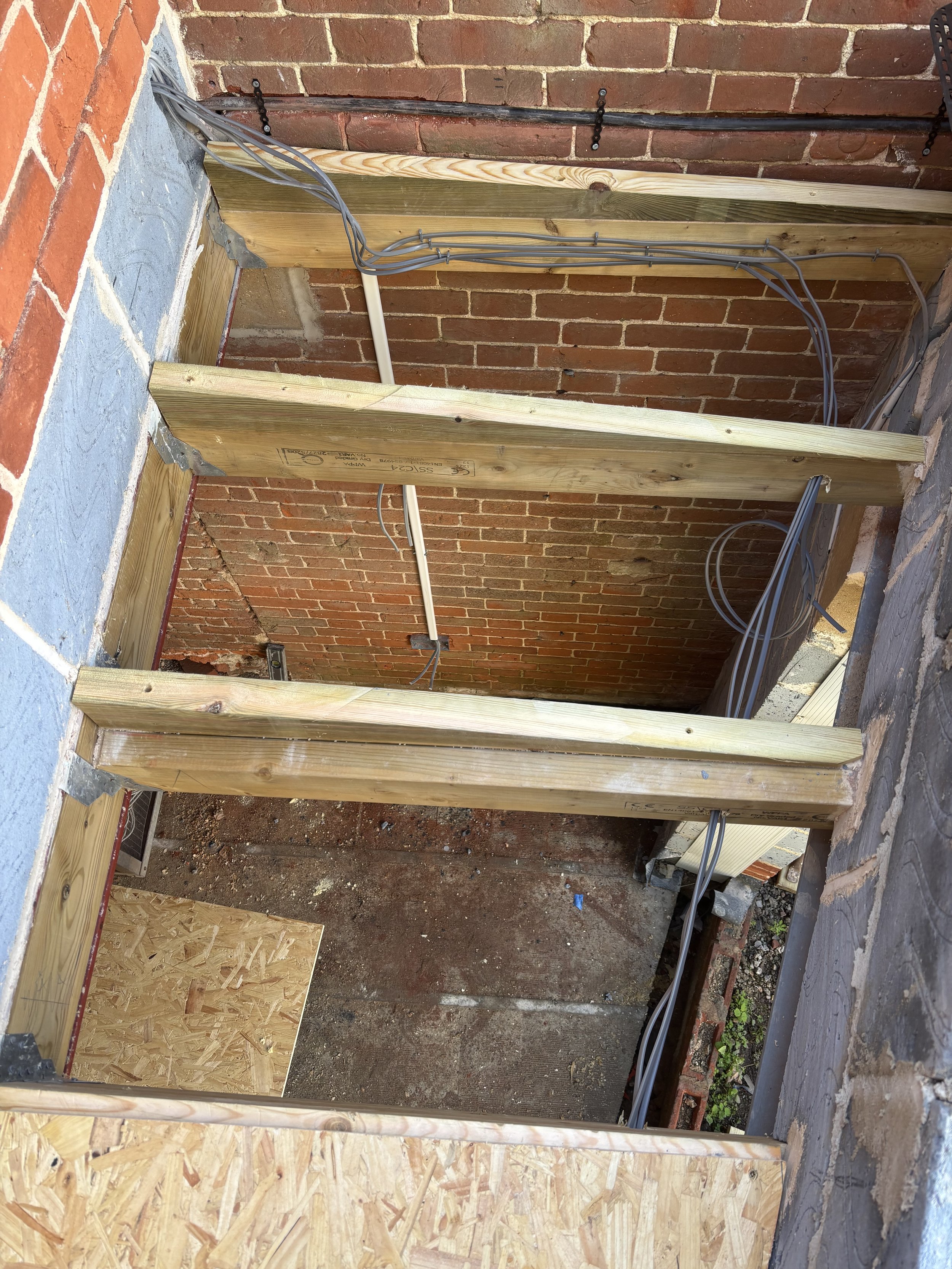 Construction site with wooden framing, electrical wires, and brick walls.