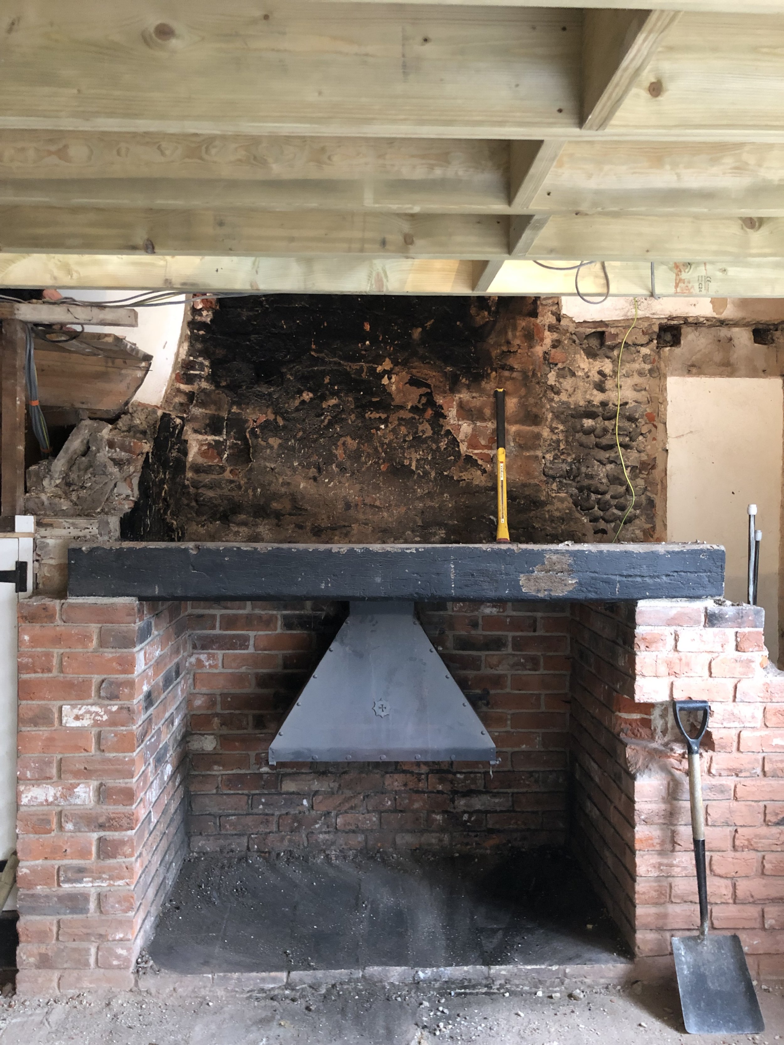 Fireplace under construction with a brick surround, a metal chimney pipe, and a metal fire grate. Tools and construction materials are visible around the fireplace.