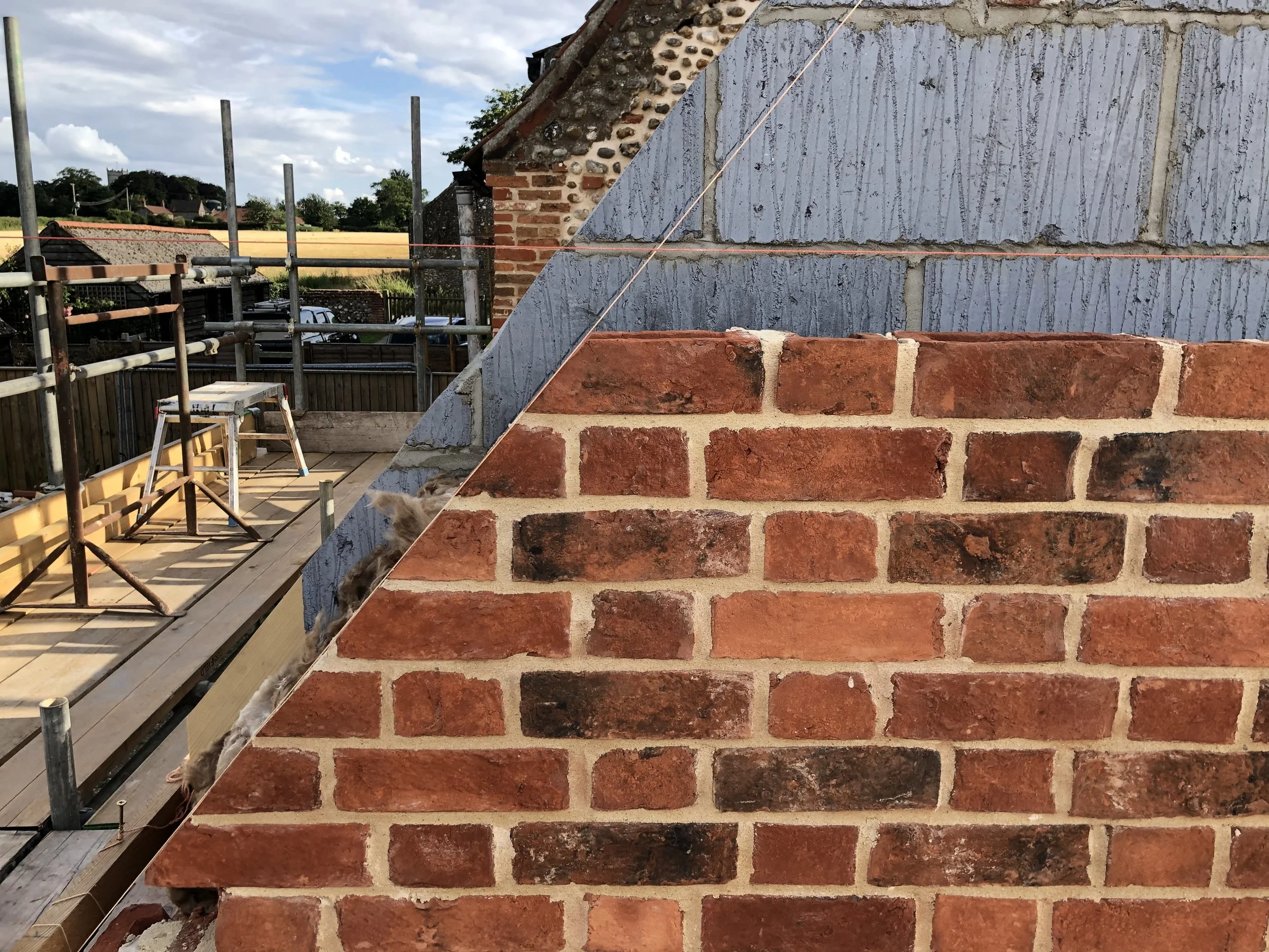 Photo of a brick wall under construction on a building, with a construction scaffold and utility pole in the background, and partly cloudy sky.