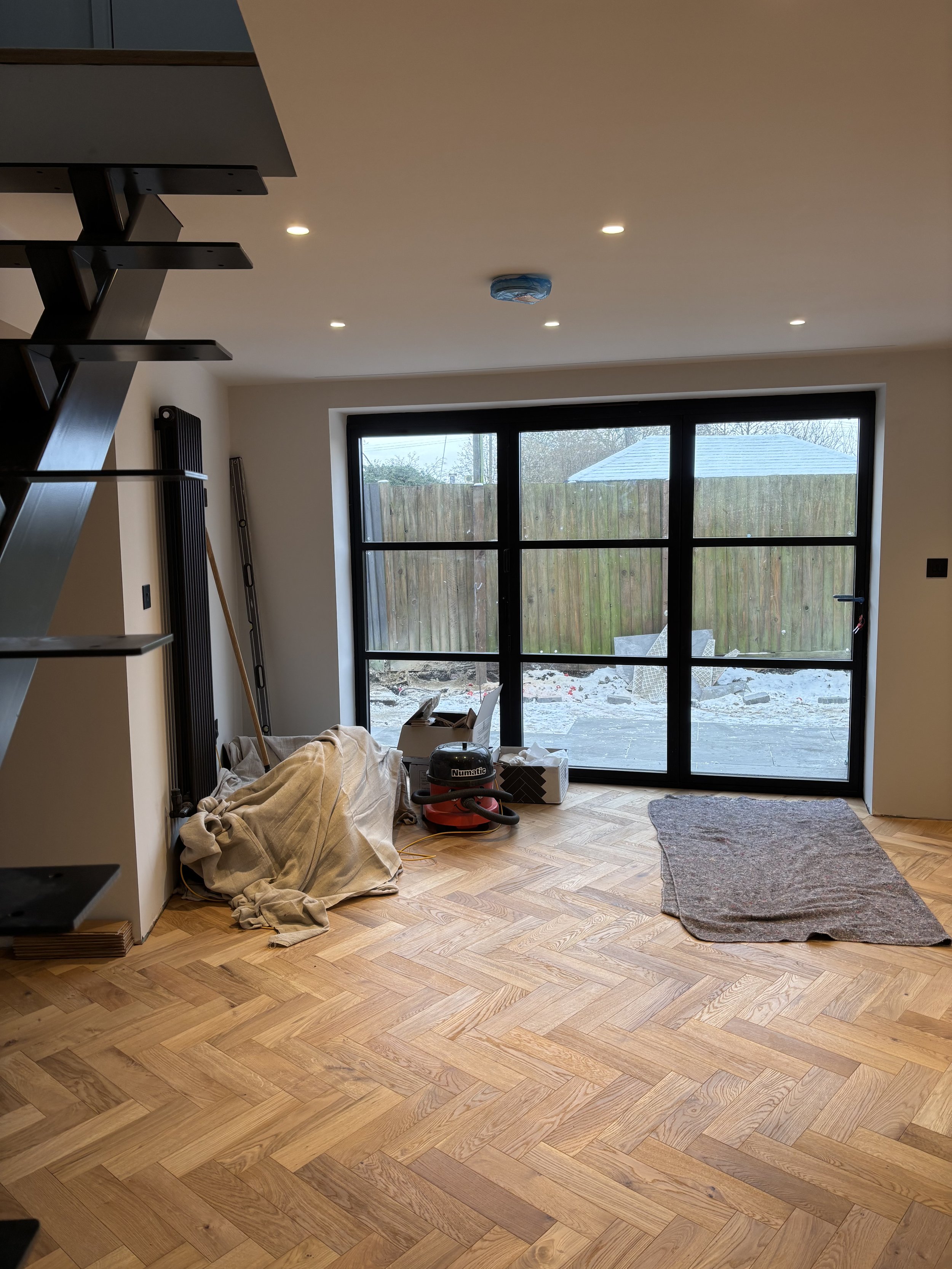 Interior view of a room with hardwood floor, large sliding glass door to outside, some tools, a vacuum, and a cloth-covered object on the floor.