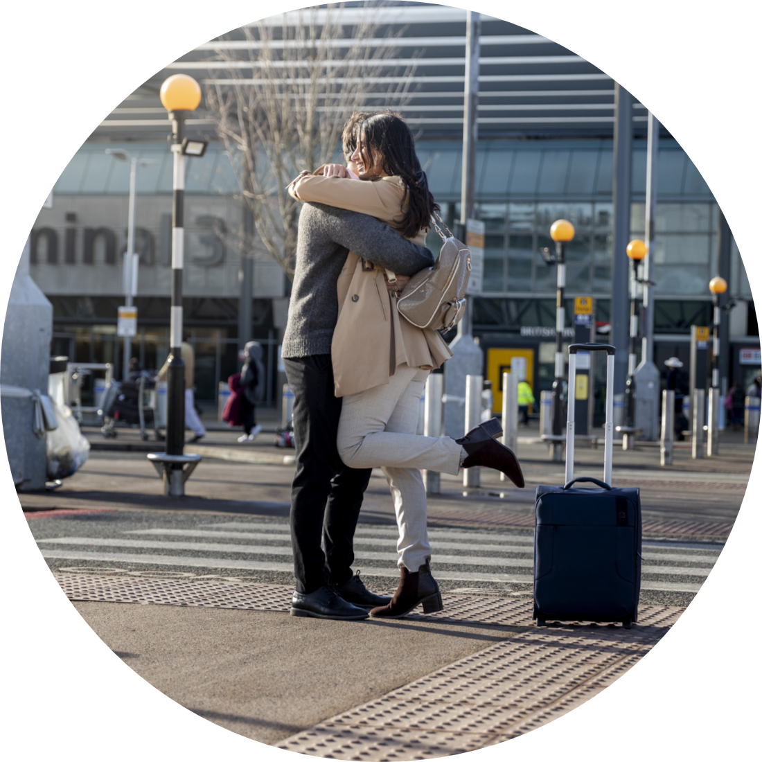 Airport transfer showing two people hugging on airport arrival area with suitcases, with the airport terminal in the background.