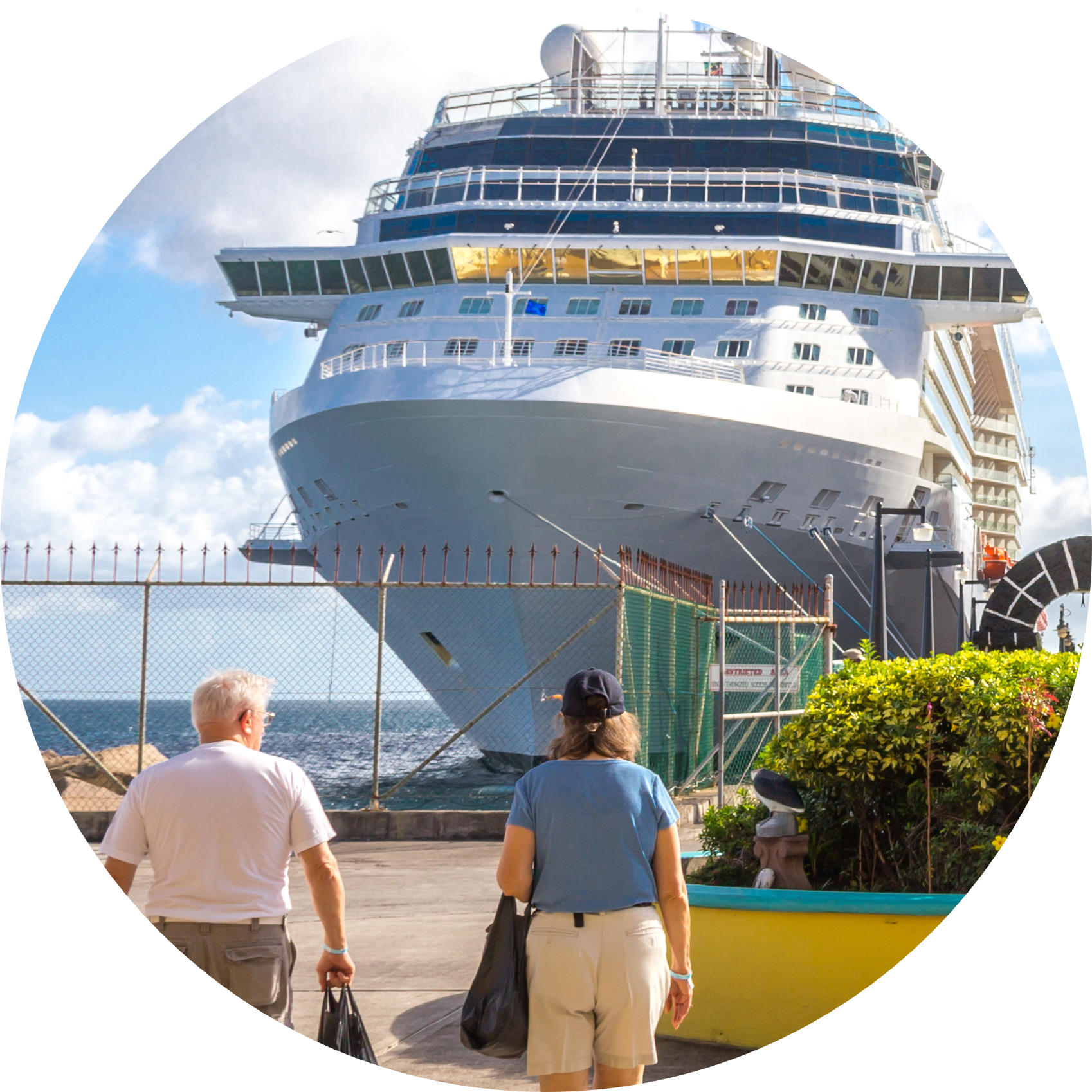 People walking in to a cruise ship docked at a port after being dropped off at a cruise terminal, sky and water visible in the background.