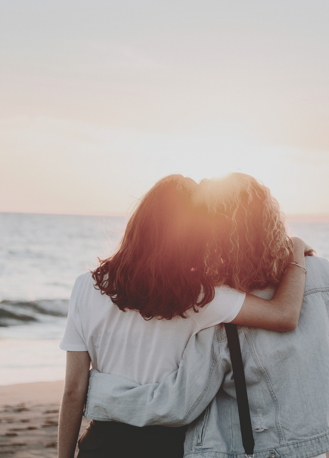 Two women embrace on the beach at sunset.
