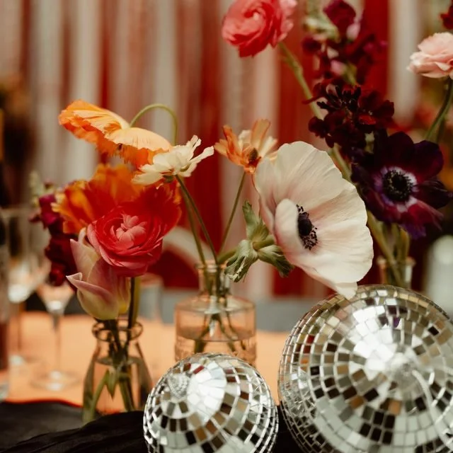 A collection of colorful flowers in vases alongside two small disco ball decorations on a table.