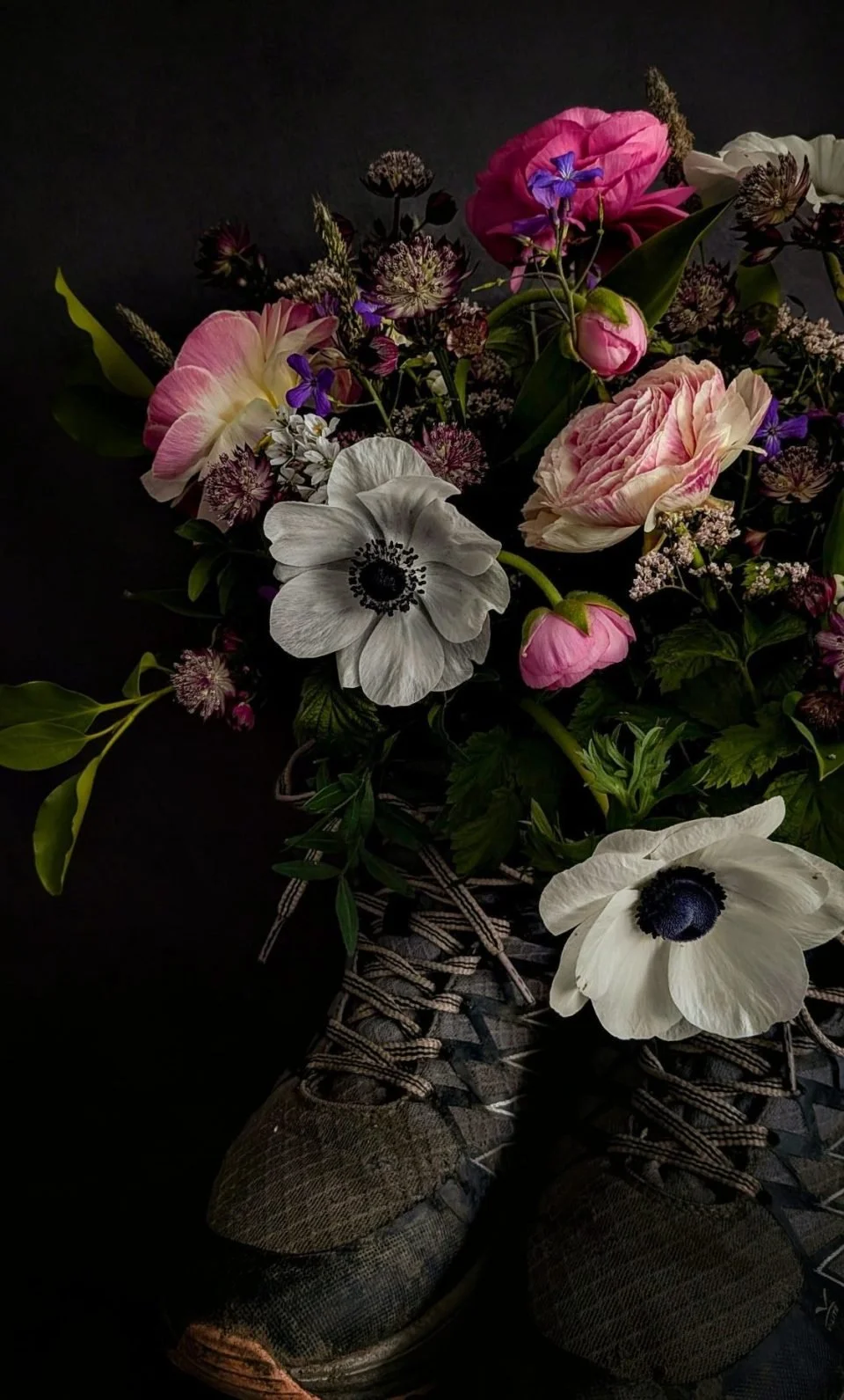 A bouquet of various colorful flowers resting on a pair of worn athletic shoes on a dark background.