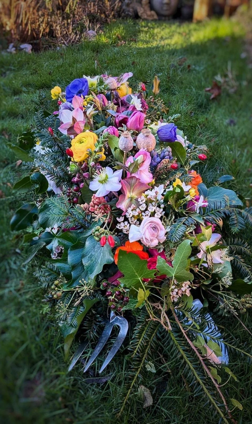 A colorful flower arrangement with various blossoms and greenery lies on grass, with garden decor in the background.