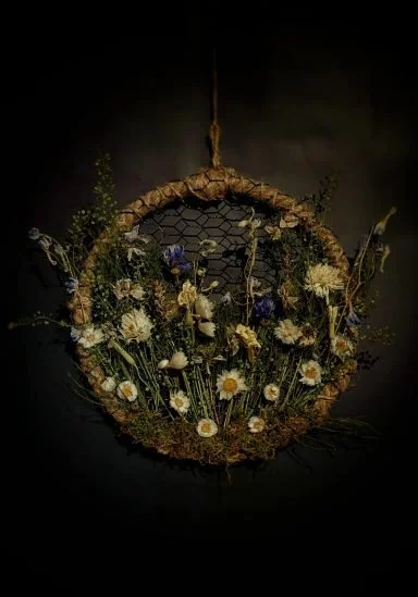 A circular hanging floral arrangement with white and purple flowers and greenery.
