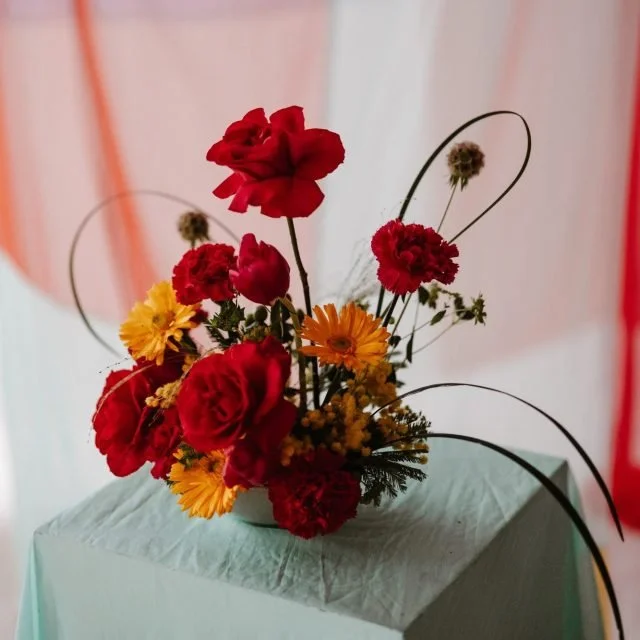 Colorful flower arrangement with red, yellow, and orange flowers in a vase on a table.