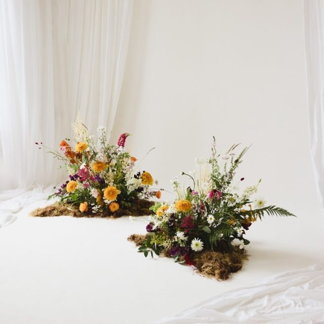 Two floral arrangements on a white surface in front of a white backdrop.
