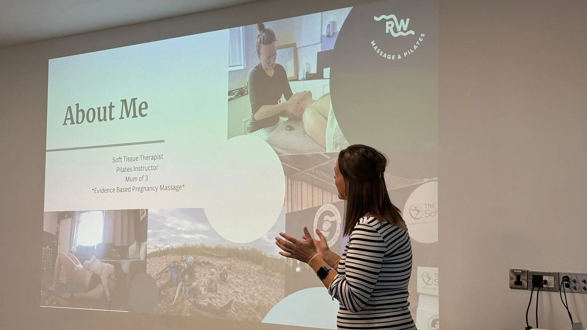 A woman in a striped shirt giving a presentation about a massage therapy business, with a slide titled 'About Me' showing her credentials and an image of her giving a massage.