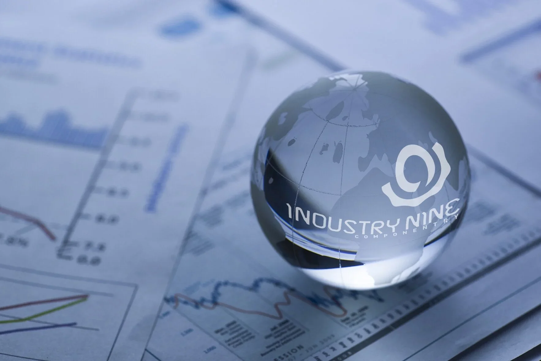 Close-up of a transparent globe with the words "Industry Nine, Country" printed on it, placed over printed financial charts and graphs.