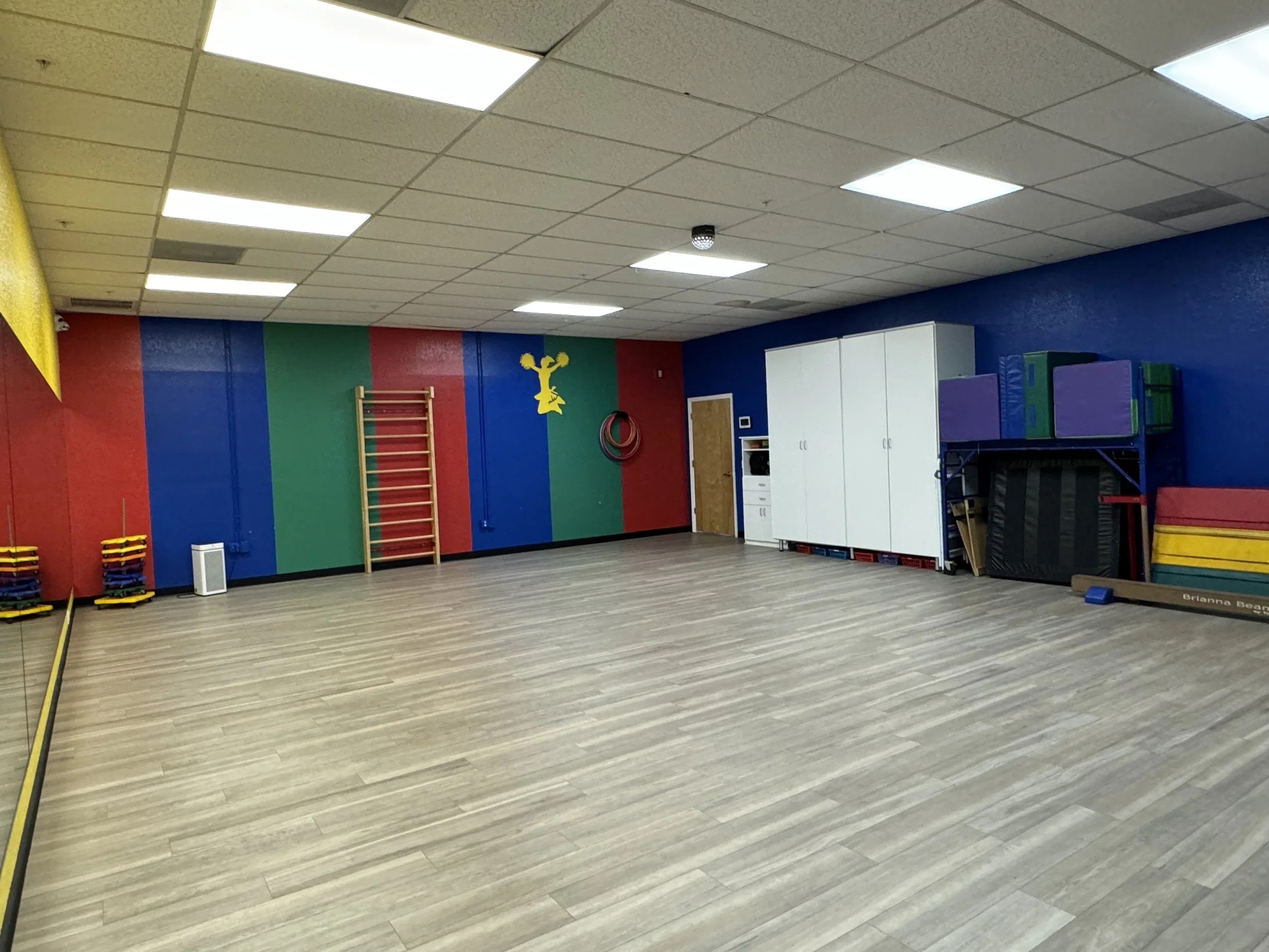 An empty indoor gym with multicolored walls, white lockers, mats, and gym equipment.