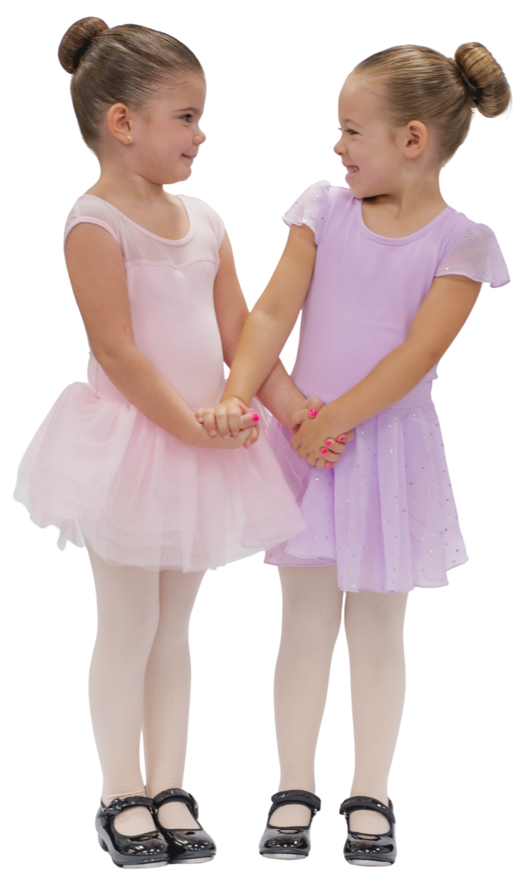 Two young girls in ballet dresses holding hands and smiling at each other