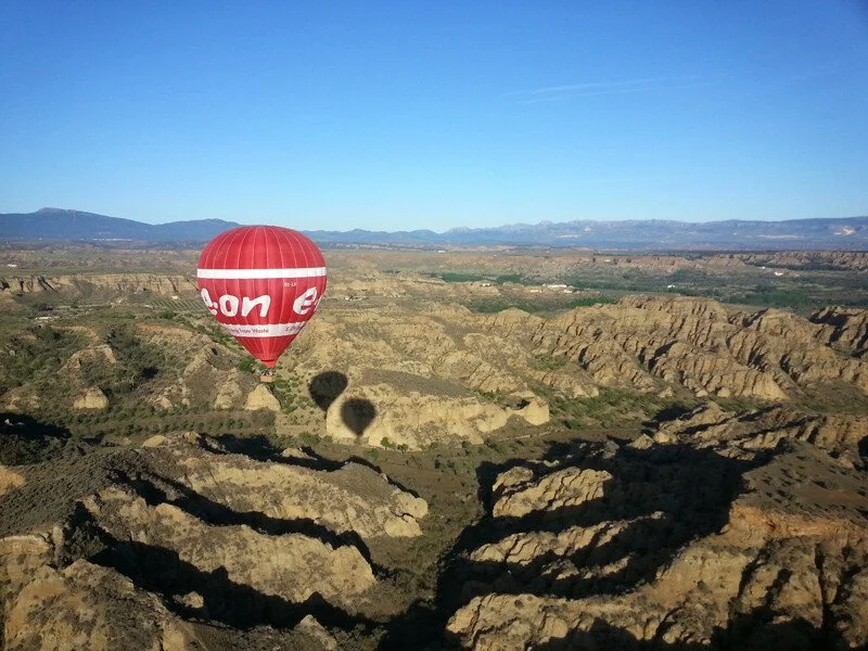 Globo aerostático rojo volando sobre un cañón rocoso, bajo un cielo despejado.