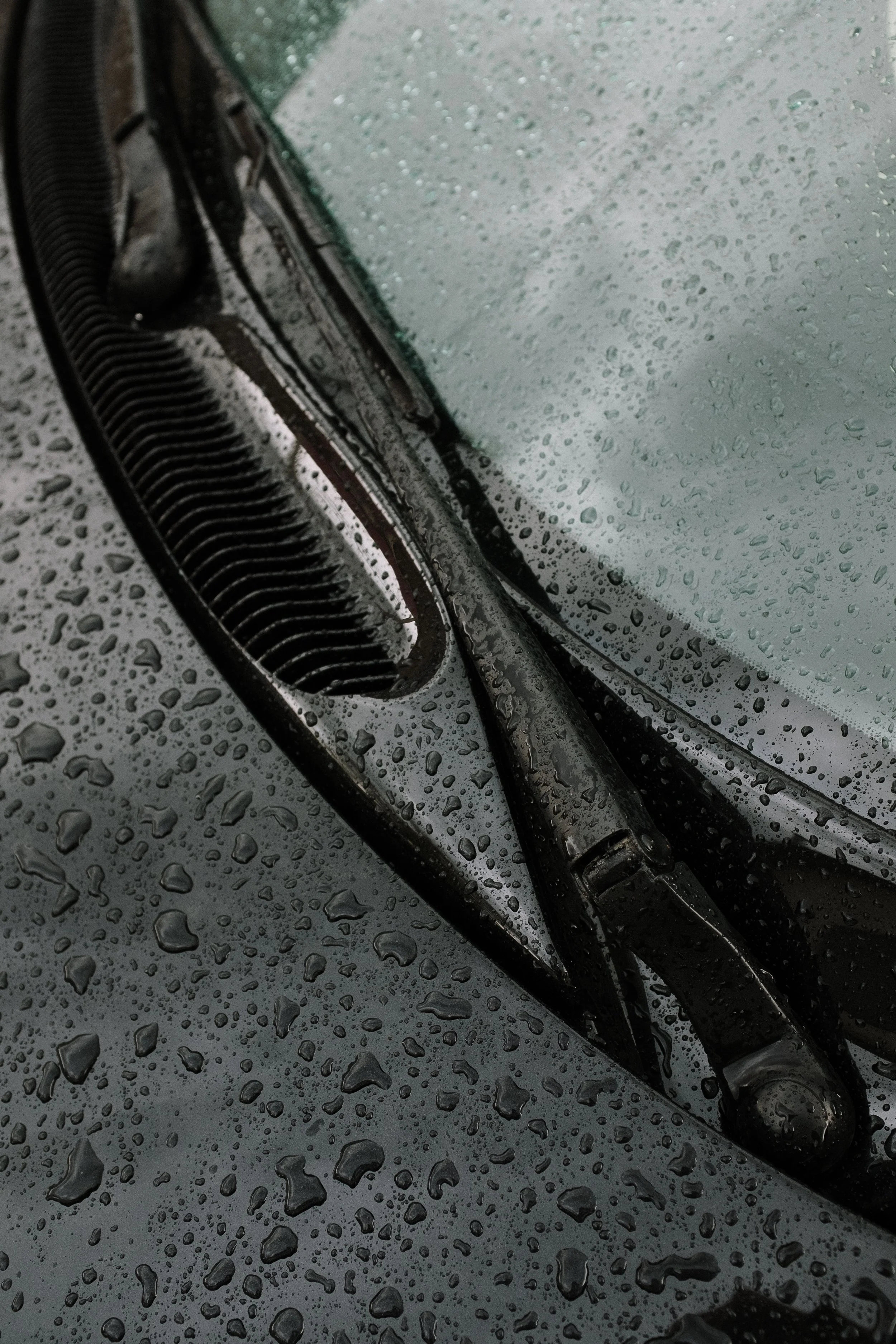 Close-up of a car's windshield wiper and windshield covered with raindrops during rainy weather.