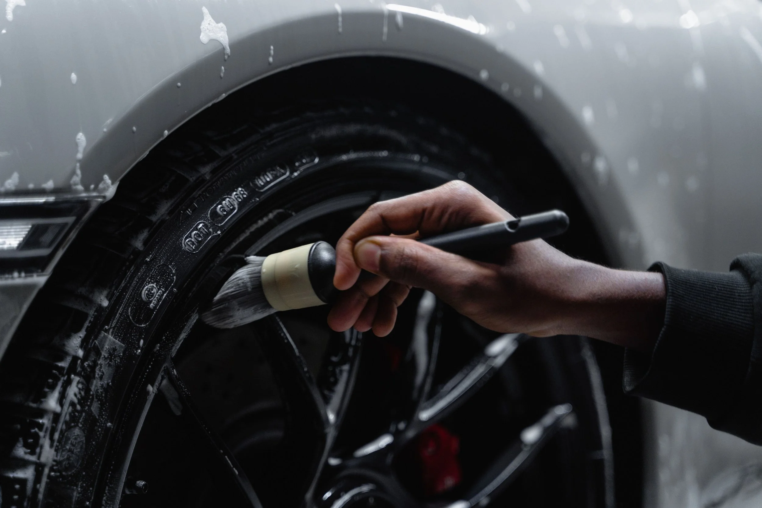 A person hand holding a wash brush cleaning the black tire of a car in a car wash or detailing shop.