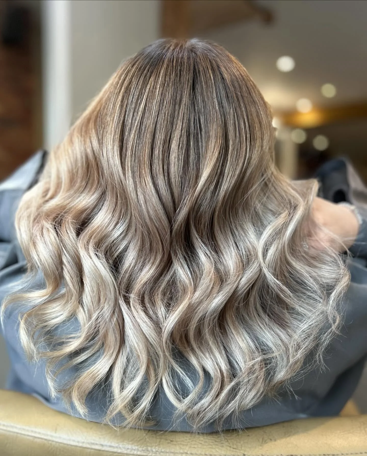 Back of a person's head with long, thick, blonde hair styled in soft waves.