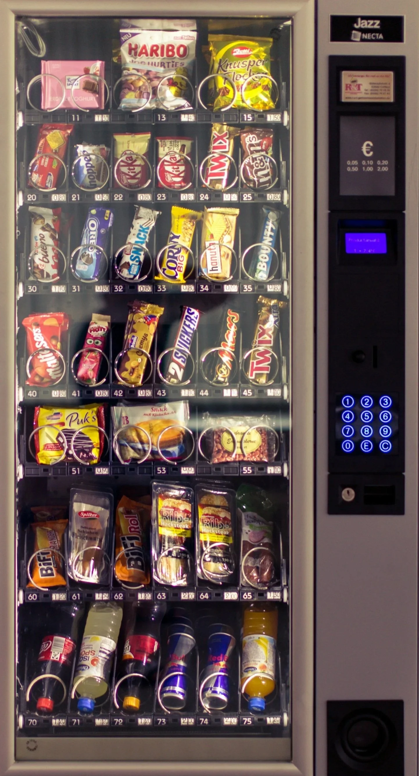 A vending machine stocked with various snacks and drinks, including candies, chocolate bars, chips, and beverages.