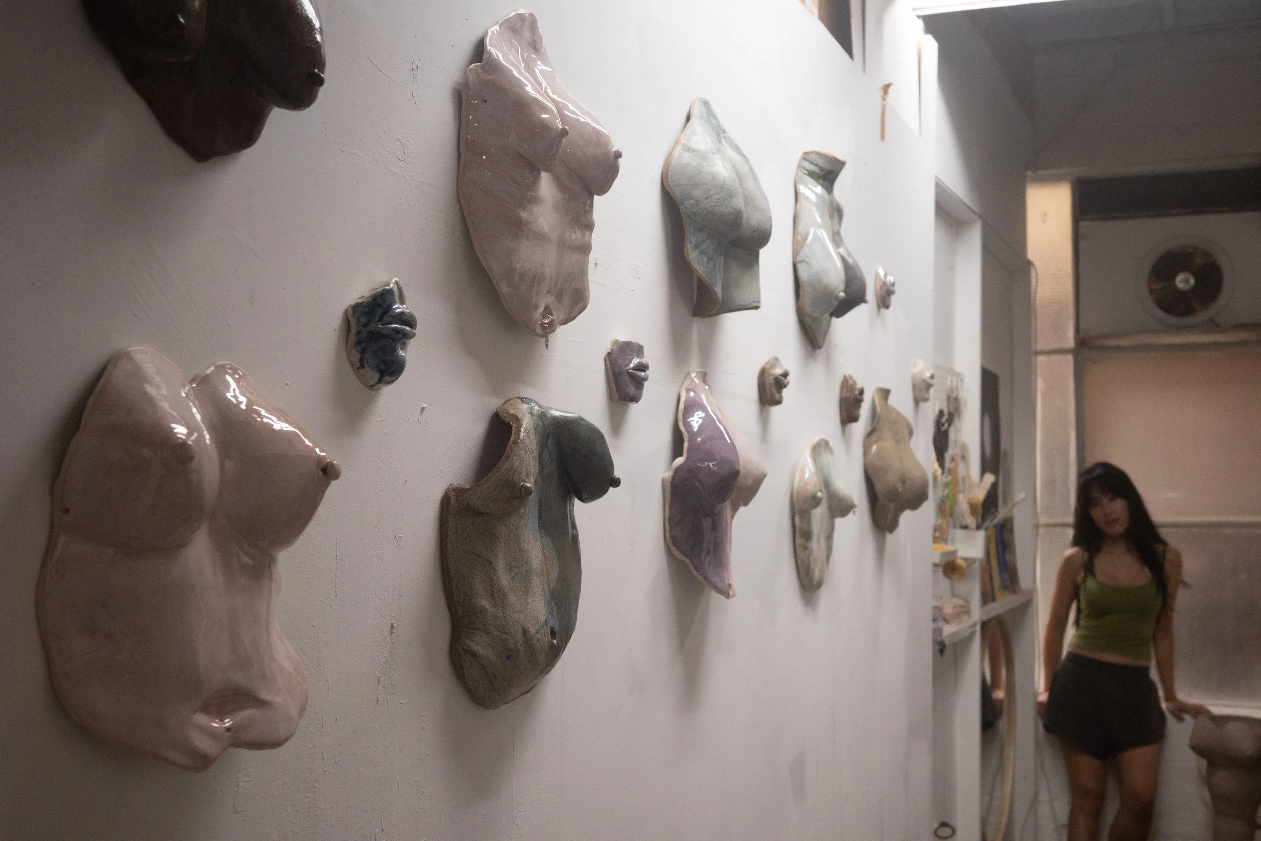 Various ceramic sculptures of human faces mounted on a white wall in an art gallery.