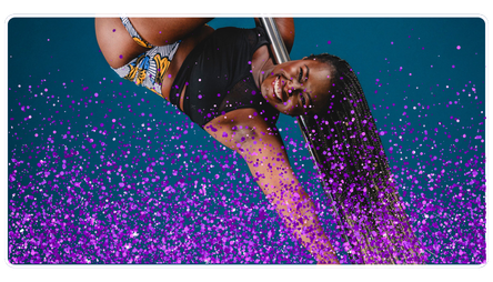 Woman performing a pole dance move on a stage with purple confetti floor.