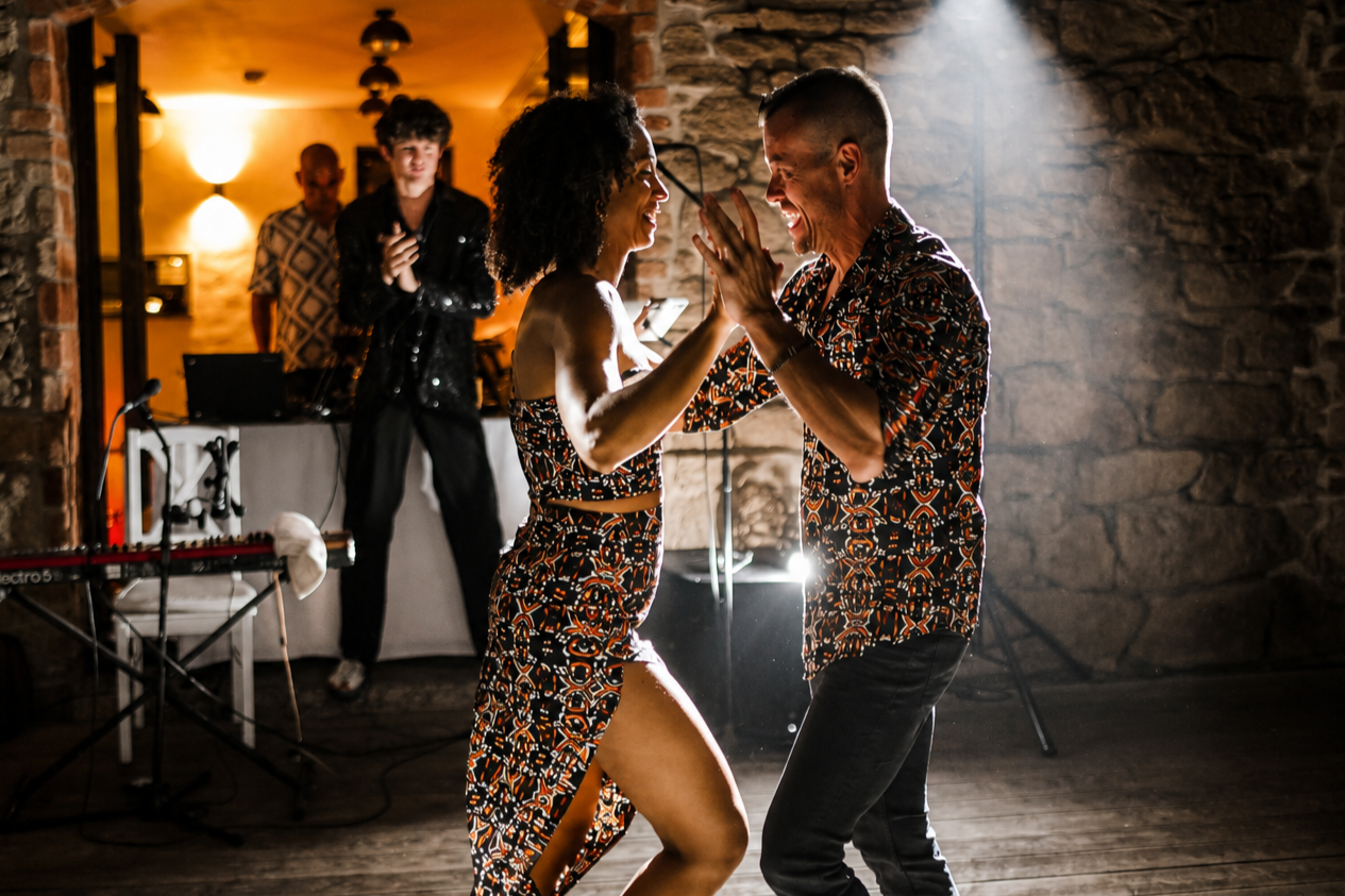 A couple dancing and smiling at an indoor party while a DJ plays music in the background.