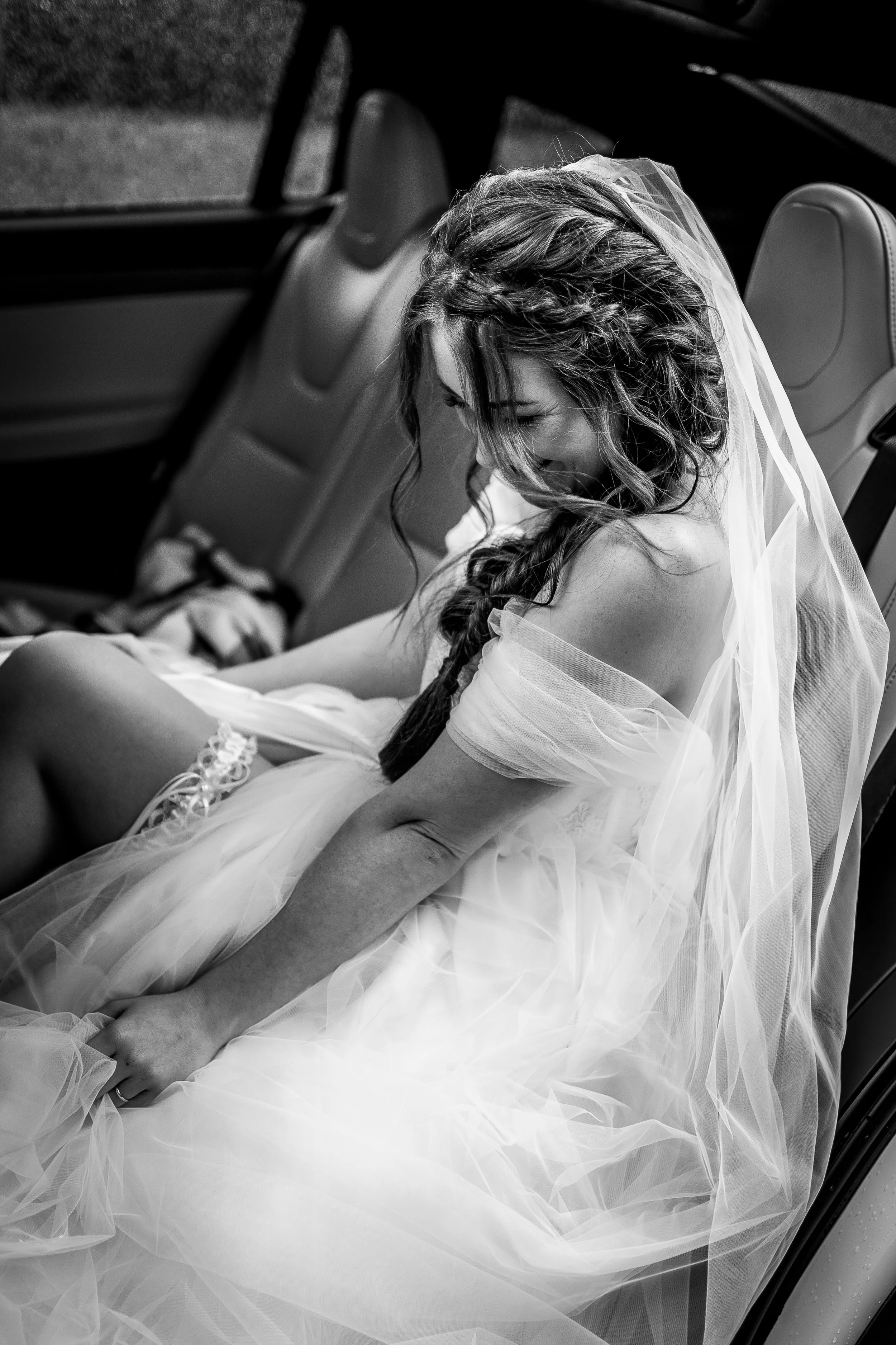 A woman in a wedding dress and veil smiling while seated in a car.