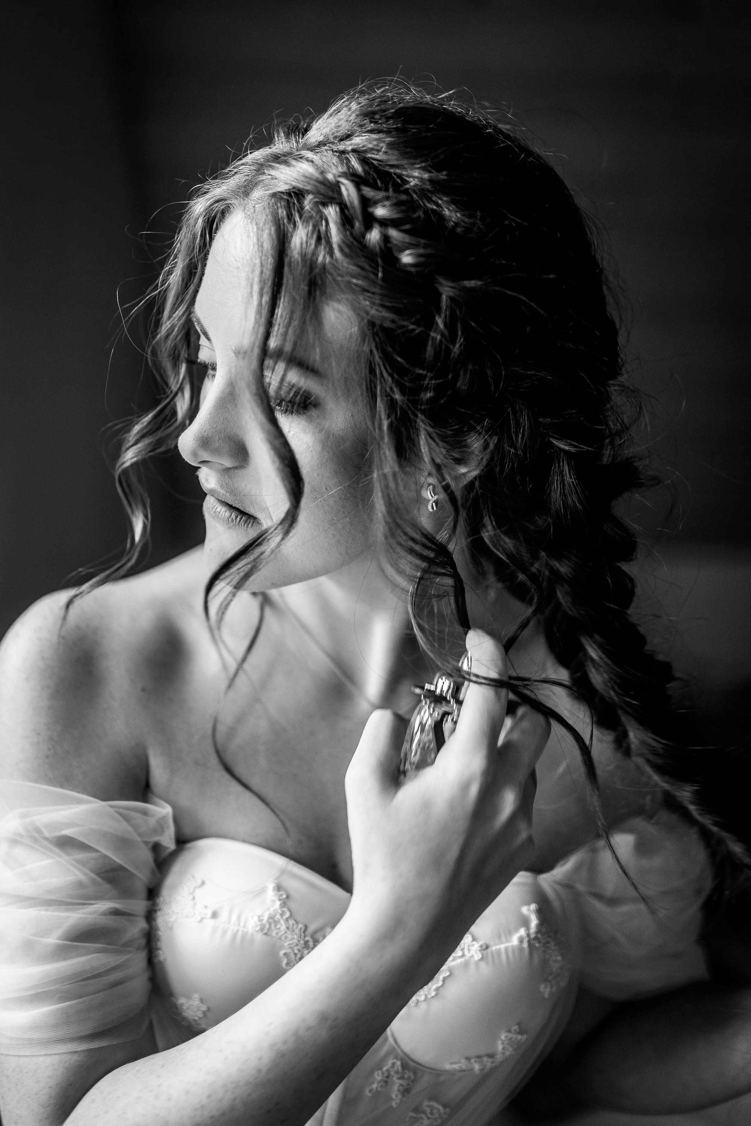 Black and white photograph of a woman with curly hair, wearing lace attire, with one eye closed and touching her face and neck, in a soft, expressive pose.