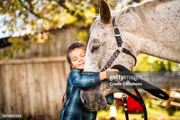 A young girl hugging a gray horse outdoors.