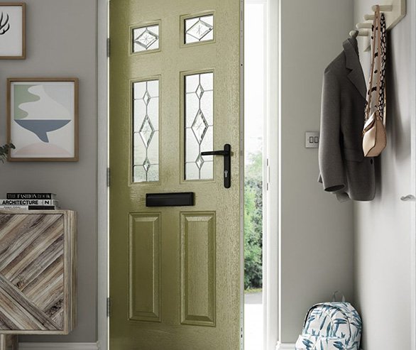 Green front door with decorative glass panels, surrounded by entryway with coat and bag hanger, artwork, and a small cabinet.