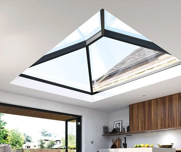 Interior view of a modern house with a large skylight ceiling allowing natural light in, showing part of the kitchen and outdoor scenery.
