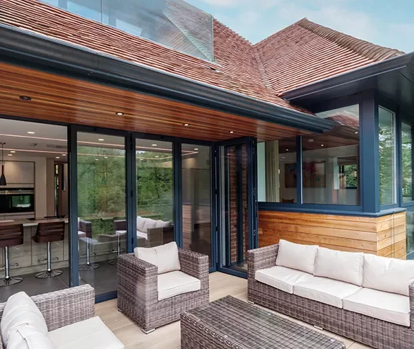 Outdoor patio with wicker furniture and glass sliding doors leading into the house, featuring a modern design with wood accents and a view of the indoor living space.