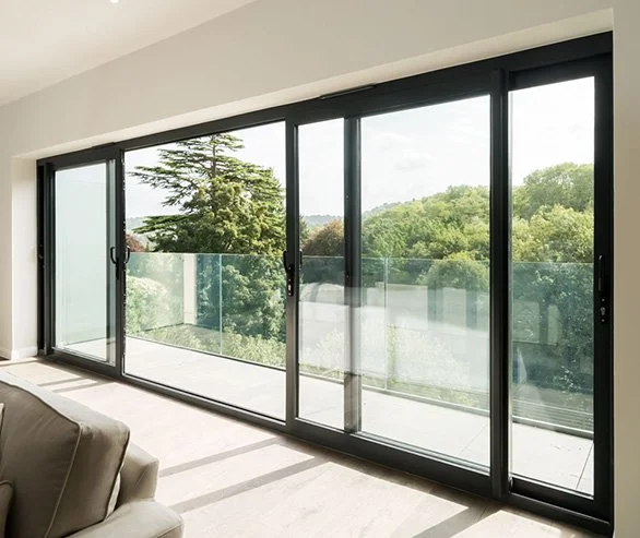 Sliding glass door leading to a balcony with a glass railing, overlooking a green scenic landscape with trees and a cloudy sky.