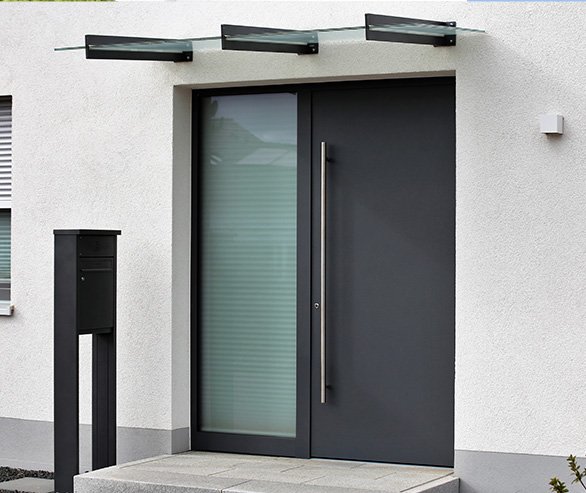 Modern front door with a large handle, glass panel, black mailbox, and three black light fixtures above the door on a white exterior wall.