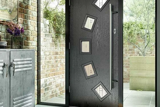 Modern black front door with five small, square windows arranged diagonally, leading to an outdoor patio with brick wall and greenery.
