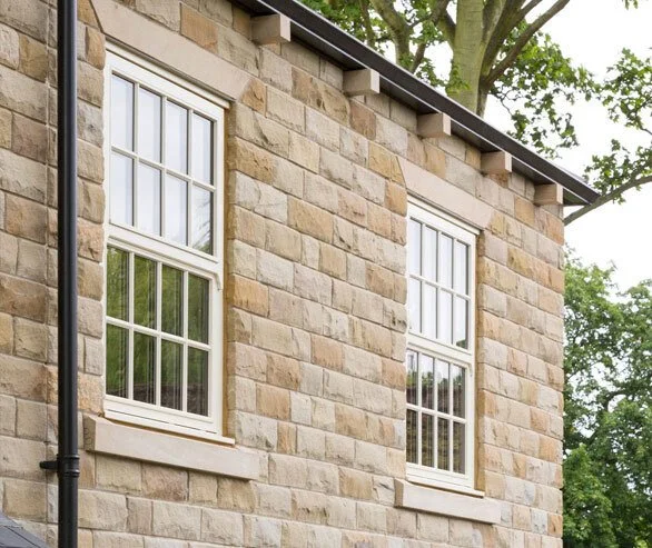 Close-up of a brick house with two white double-hung windows and a black downspout on the left side.