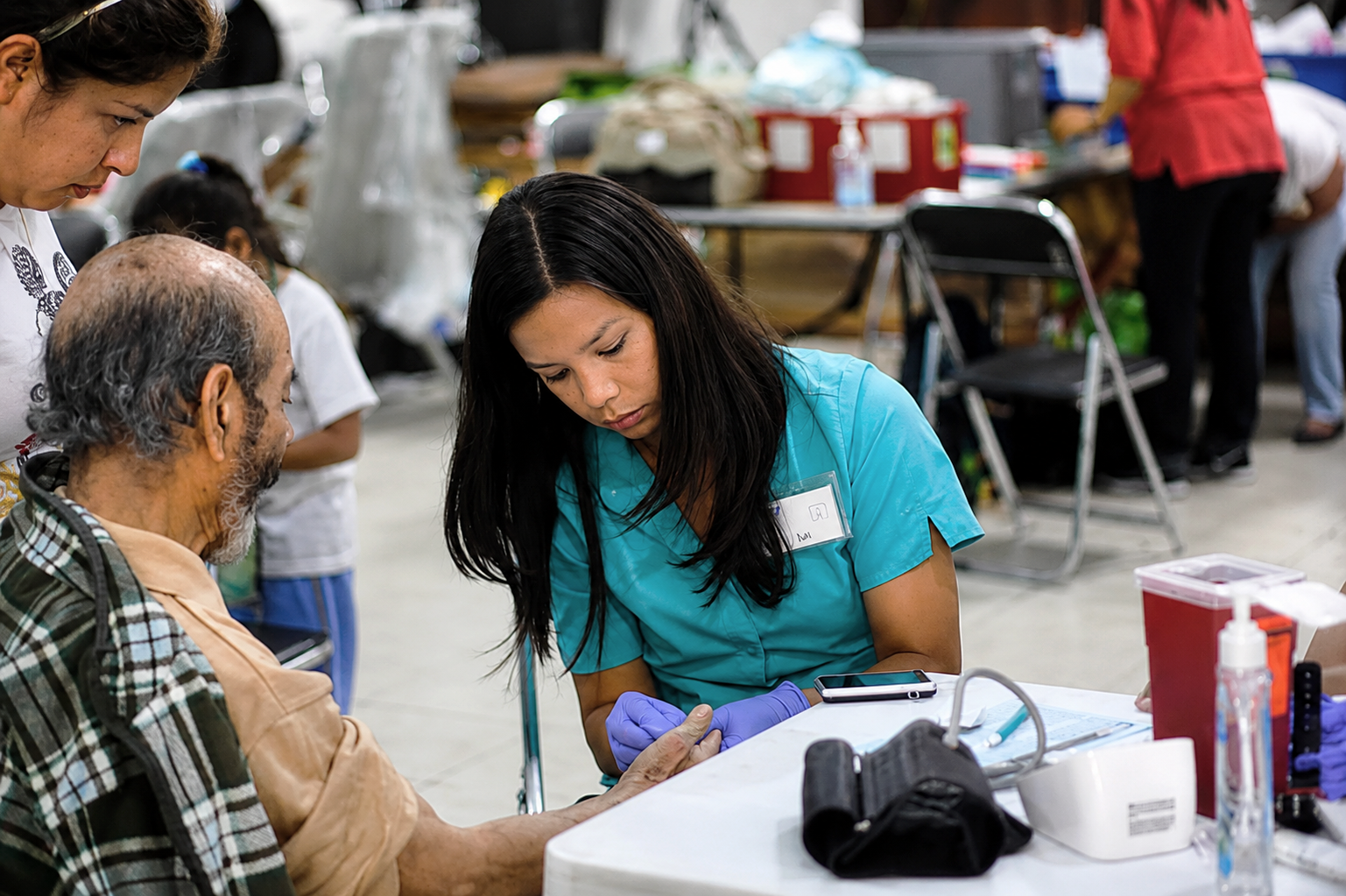Young medical professional examining an old man's hand at OSI's clinical outreach