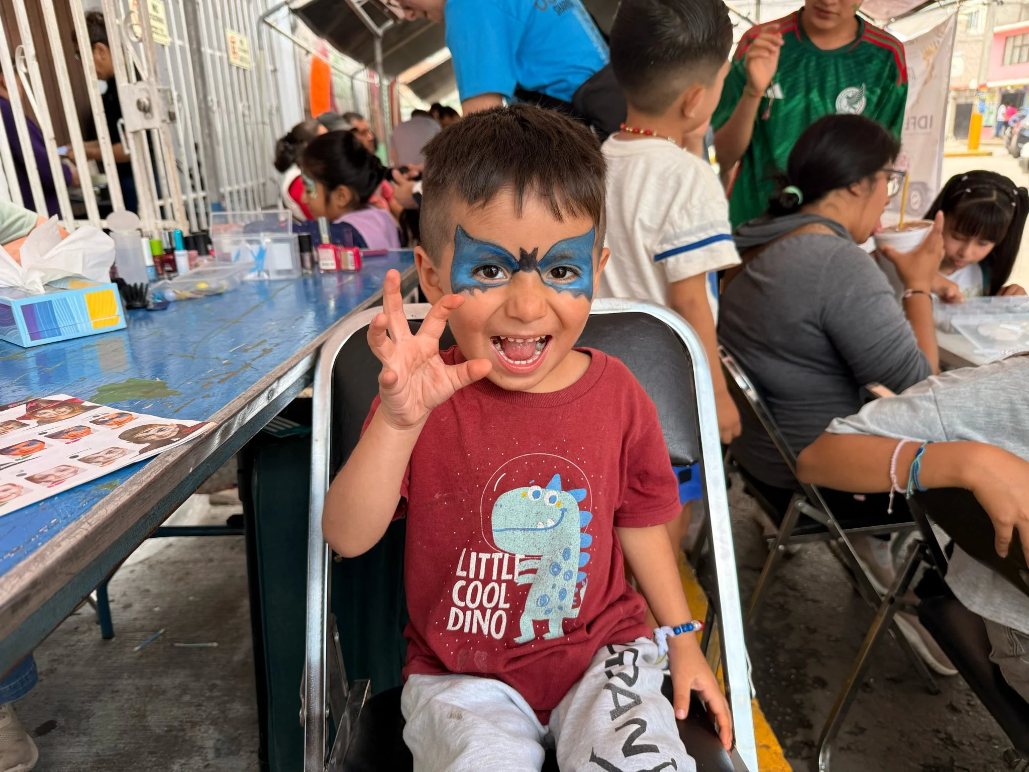 Young boy smiling with superhero face paint during a community outreach event.