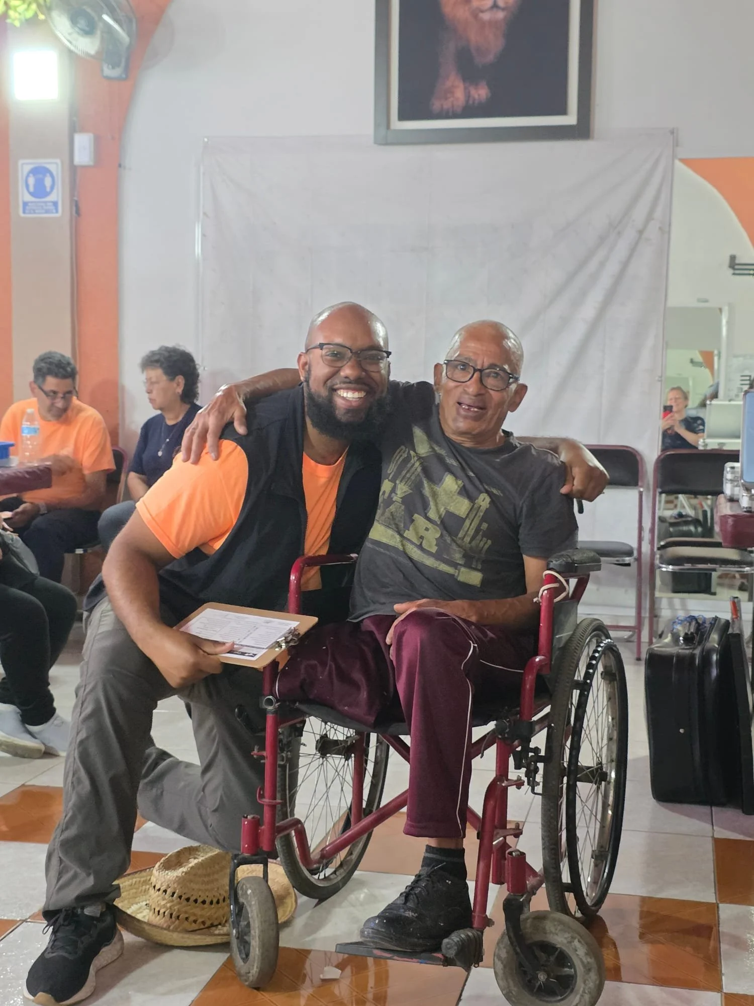 OSI volunteer, Russell smiling with a man in a wheelchair he just assisted