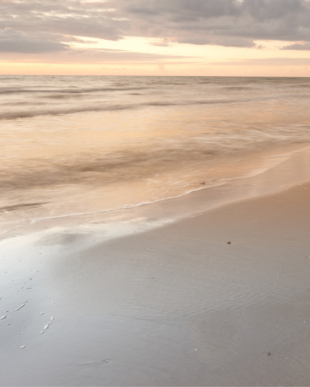 Sunset over the ocean with gentle waves lapping onto a sandy beach.