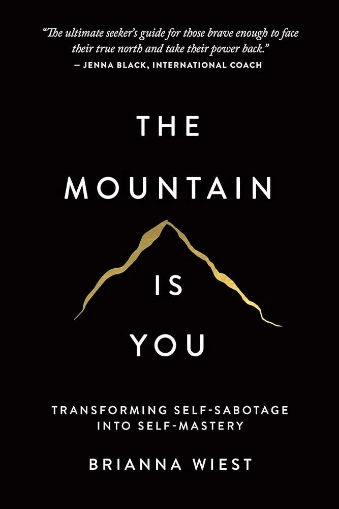 Book cover with a black background, featuring a gold outline of a mountain and white text, including a quote, title 'The Mountain is You,' subtitle about transforming self-sabotage into self-mastery, and author Brianna Wiest.