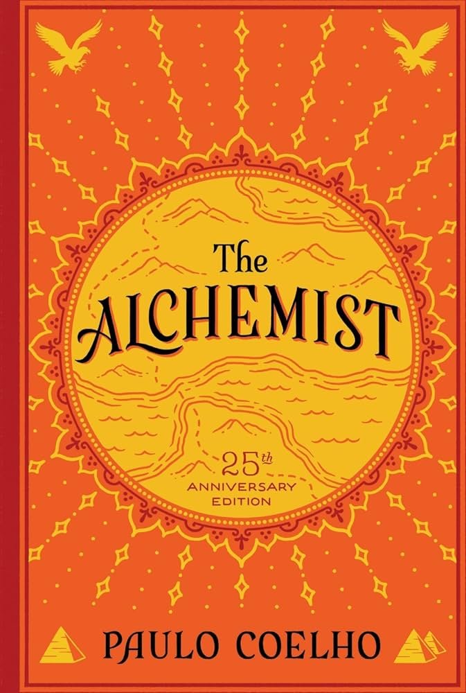 Book cover for 'The Alchemist' by Paulo Coelho, 25th anniversary edition, featuring a bright orange background with yellow and red decorative elements, a central circular design resembling a map or landscape, and two stylized golden eagles at the top corners.