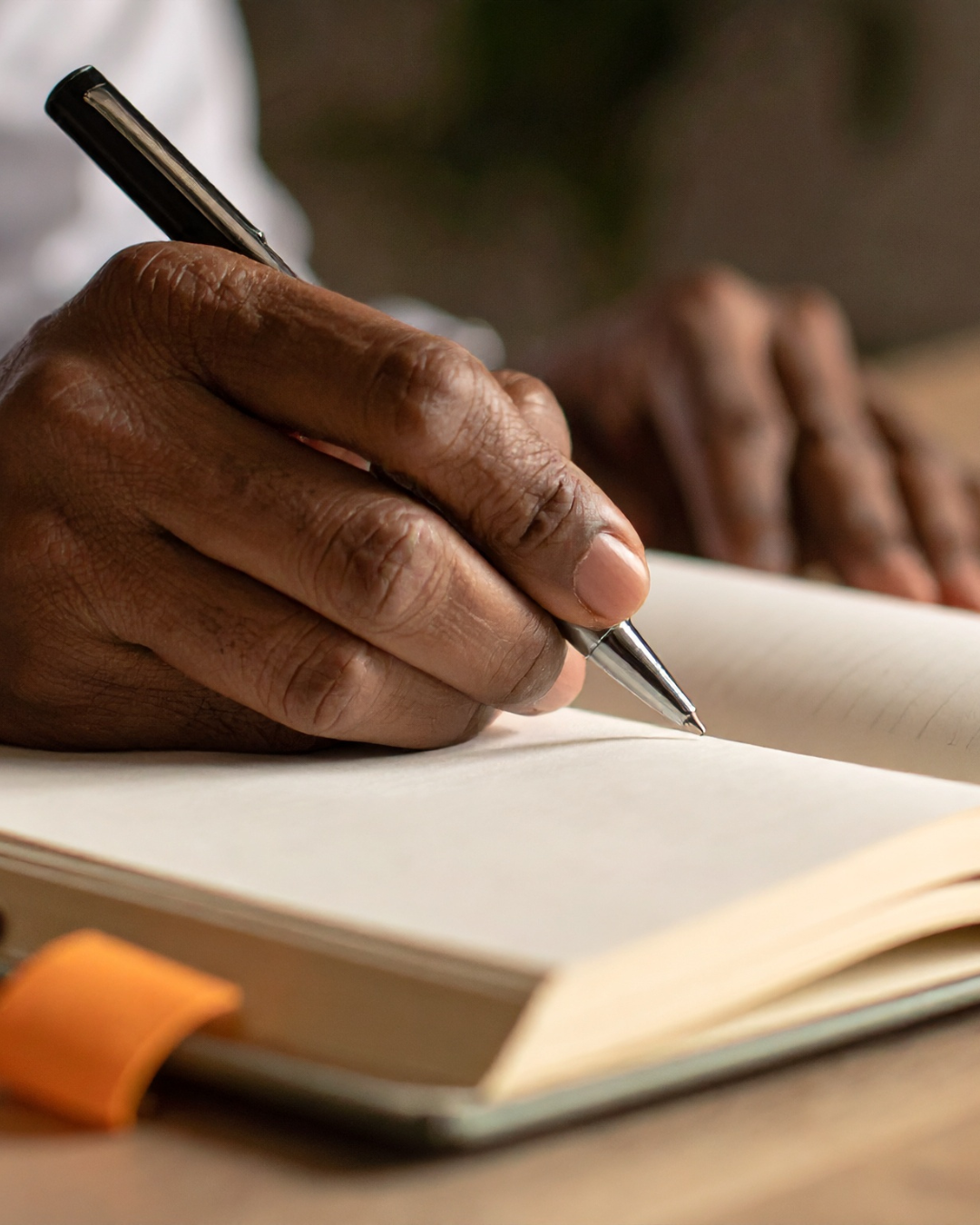 A person writes in a notebook with a silver and black pen, focusing on their hand and the writing process.