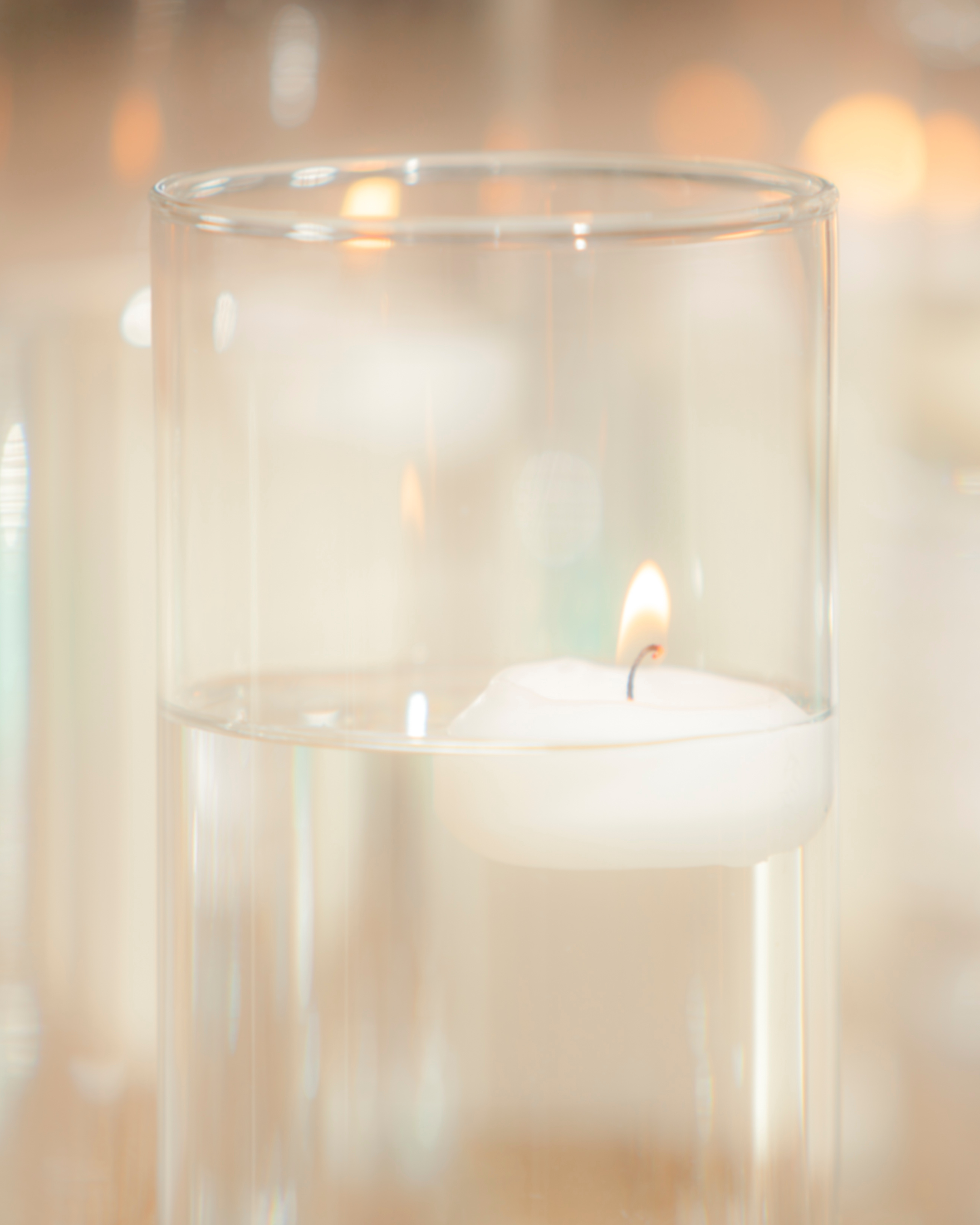 Close-up view of a glass container, possibly a candle holder, with a lit candle inside. The background is blurred with warm, golden bokeh lights.