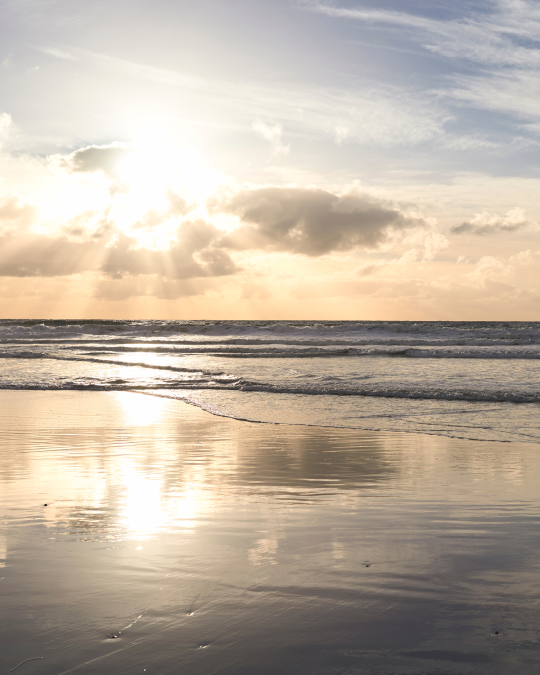 Sunset over the ocean with clouds and waves, reflection on wet sand.