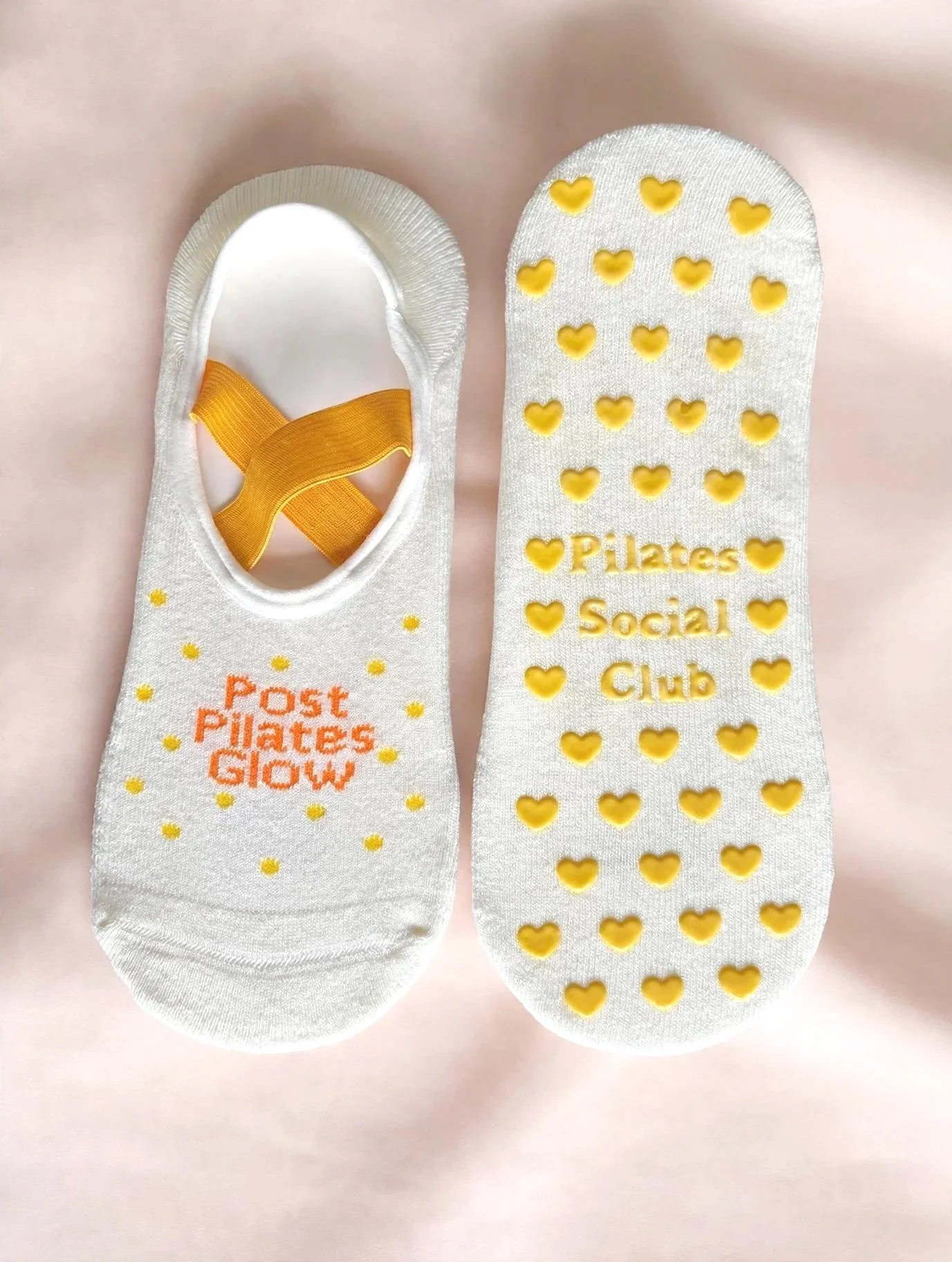 Cream base with Warm Yellow "Post Pilates Glow'" text, in a ballet style with yellow straps to keep them in place. Yellow Polka dots scattered on the front and  Non-slip heart shaped Grips on the base, the perfect sock for Pilates, Yoga and Barre